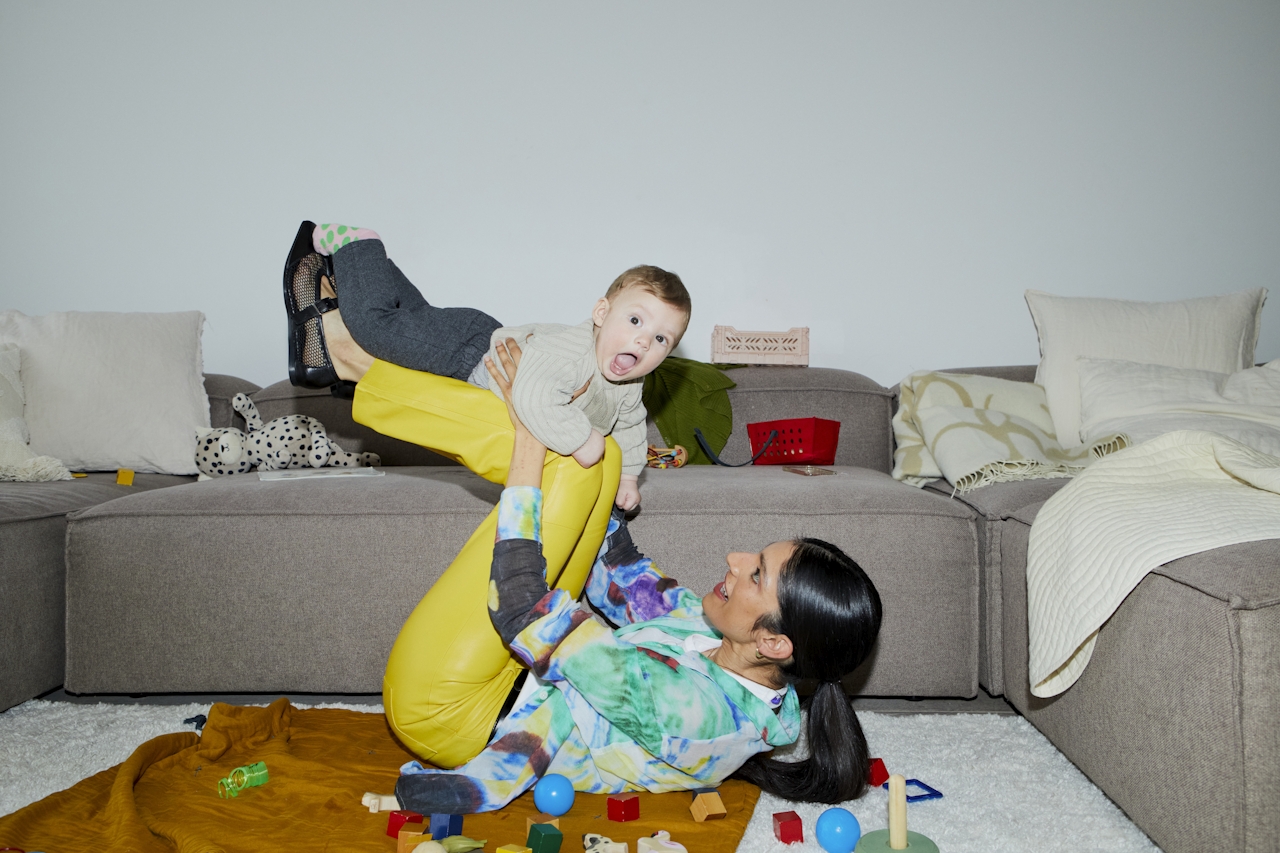A parent lying on the floor lifting a laughing toddler in a toy-filled living room