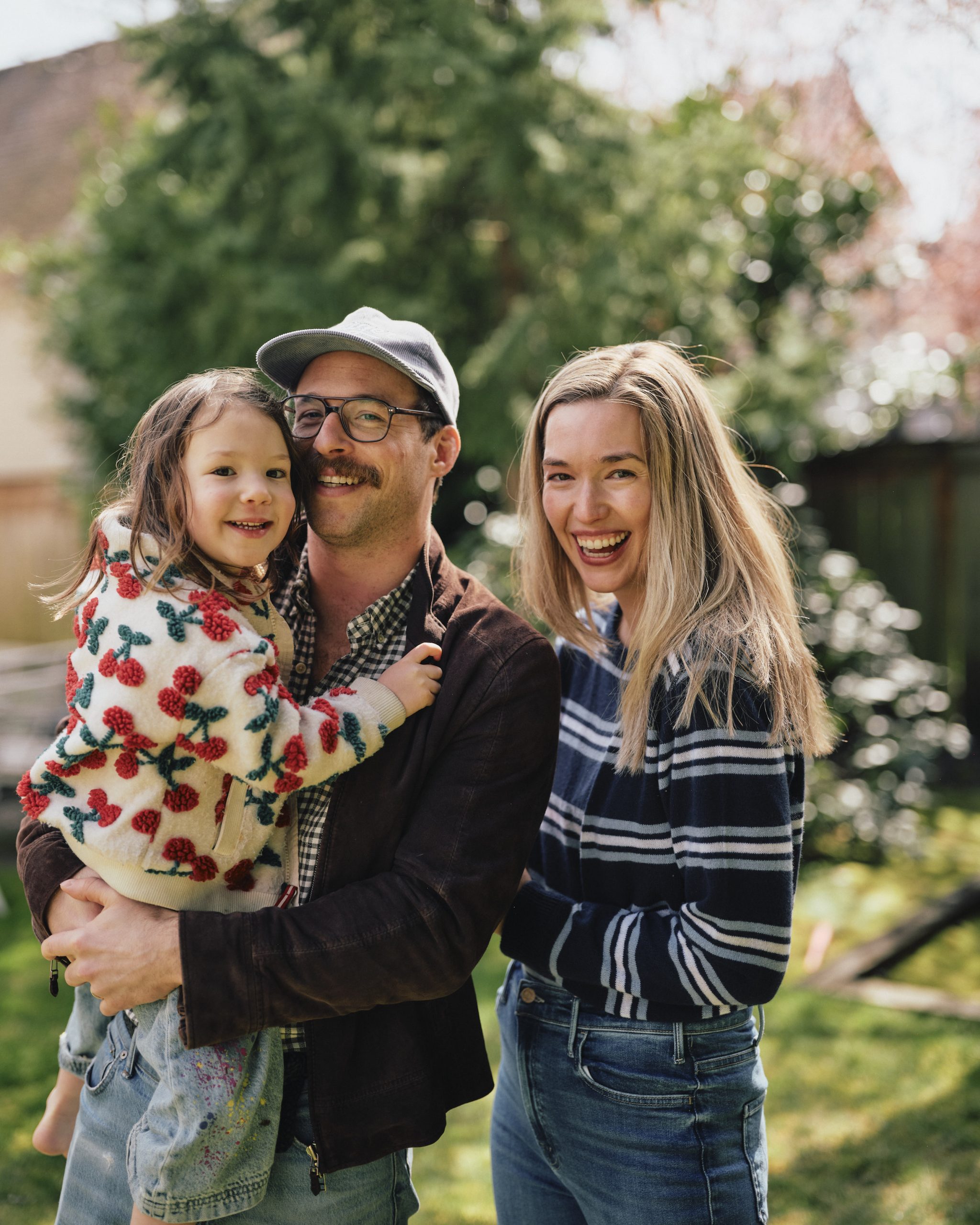 A smiling young family with a child in a sunlit backyard